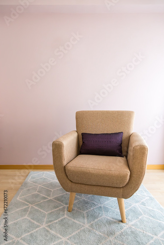One-seater armchair with cushion on light blue carpet, wooden floor and pastel pink wall. Natural light. Concept of empty chair, minimalism, solitude, listening space. Copy space