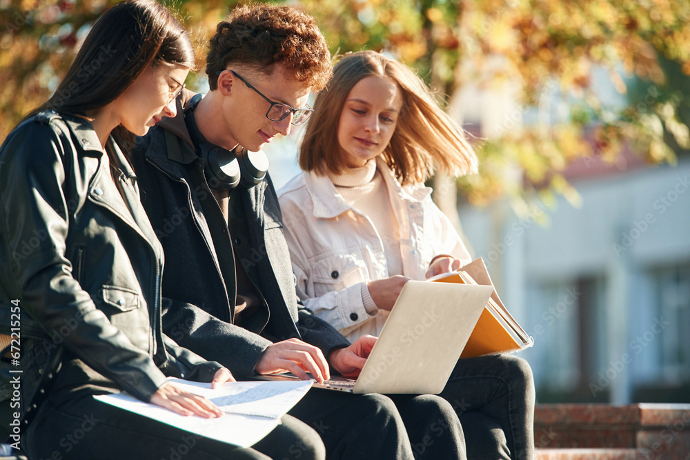 Learning, sitting and using laptop. Three young students are outside the university outdoors Learning, sitting and using laptop. Three young students are outside the university outdoors