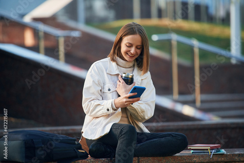 Smartphone in hands. Young female student in casual clothes is outdoors