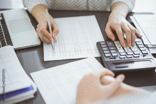Woman accountant using a calculator and laptop computer while counting taxes with a client or a colleague. Business audit team, finance advisor