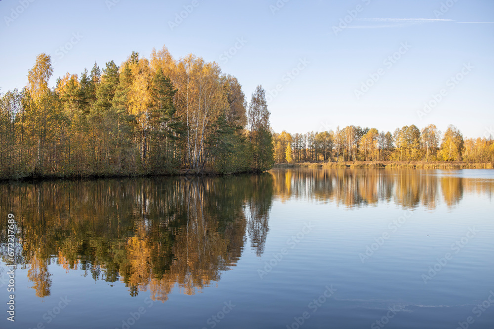 Autumn landscape with a pond. Trees with yellow foliage are reflected in the water.