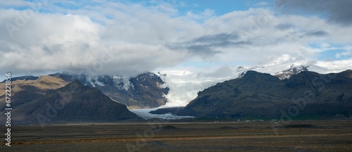 Scenic winter landscape featuring a range of snow-capped mountains against a partially cloudy sky.