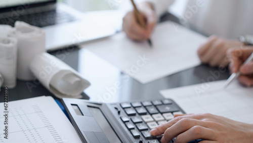 Two accountants use a calculator and laptop computer for counting taxes or revenue balance. Business, audit, and taxes concepts