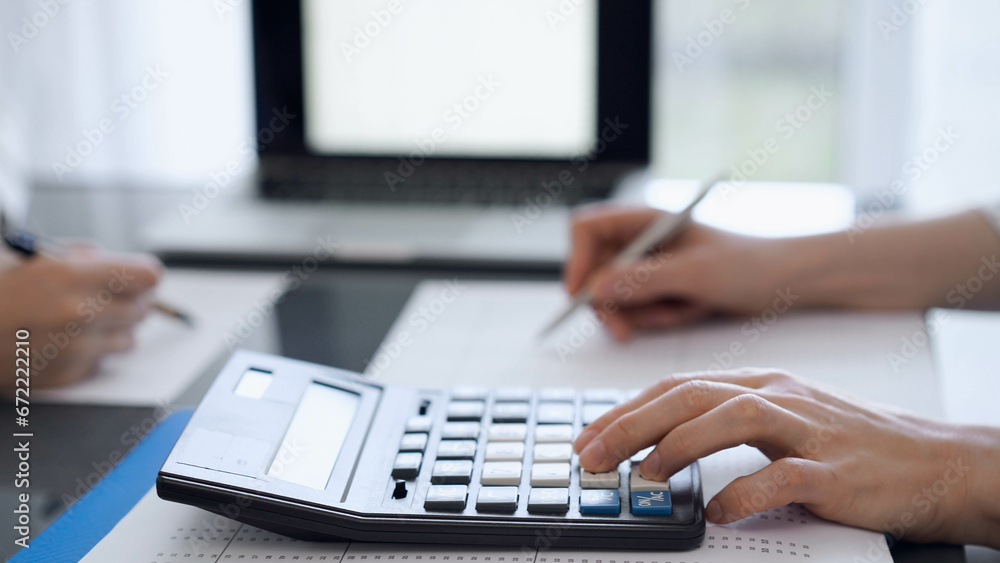 Two accountants use a calculator and laptop computer for counting taxes or revenue balance. Business, audit, and taxes concepts Two accountants use a calculator and laptop computer for counting taxes or revenue balance. Business, audit, and taxes concepts
