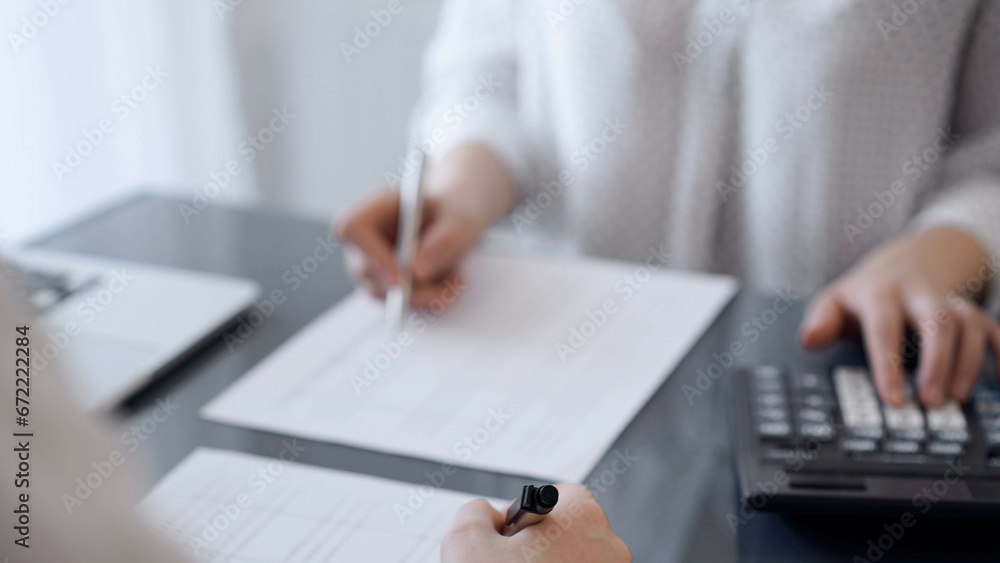 Two accountants use a calculator and laptop computer for counting taxes or revenue balance. Business, audit, and taxes concepts Two accountants use a calculator and laptop computer for counting taxes or revenue balance. Business, audit, and taxes concepts