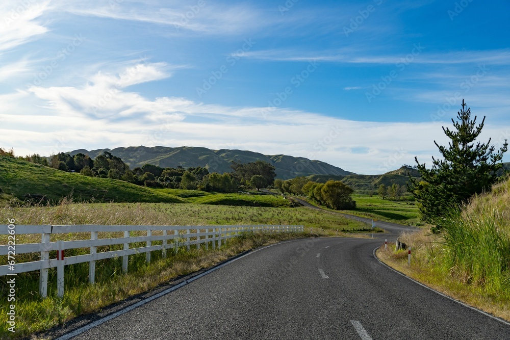 Rural road surrounded by a white picket fence and lush green grass.