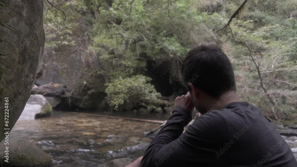 Young man taking time at riverbank to watch the flowing water and think Young man taking time at riverbank to watch the flowing water and think