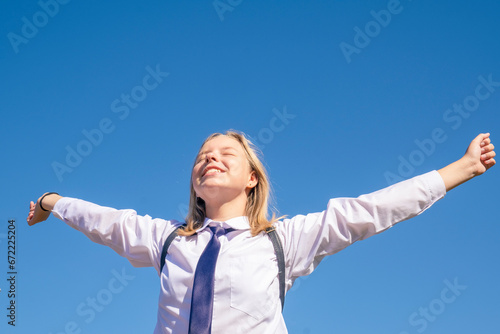 Happy girl breathing fresh air raising arms over blue sky. Girl relaxing after school. Freedom concept