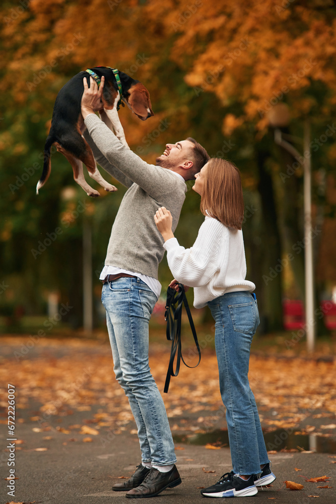 Fototapeta premium Man is holding animal high up in the hands. Lovely couple are with their cute dog outdoors