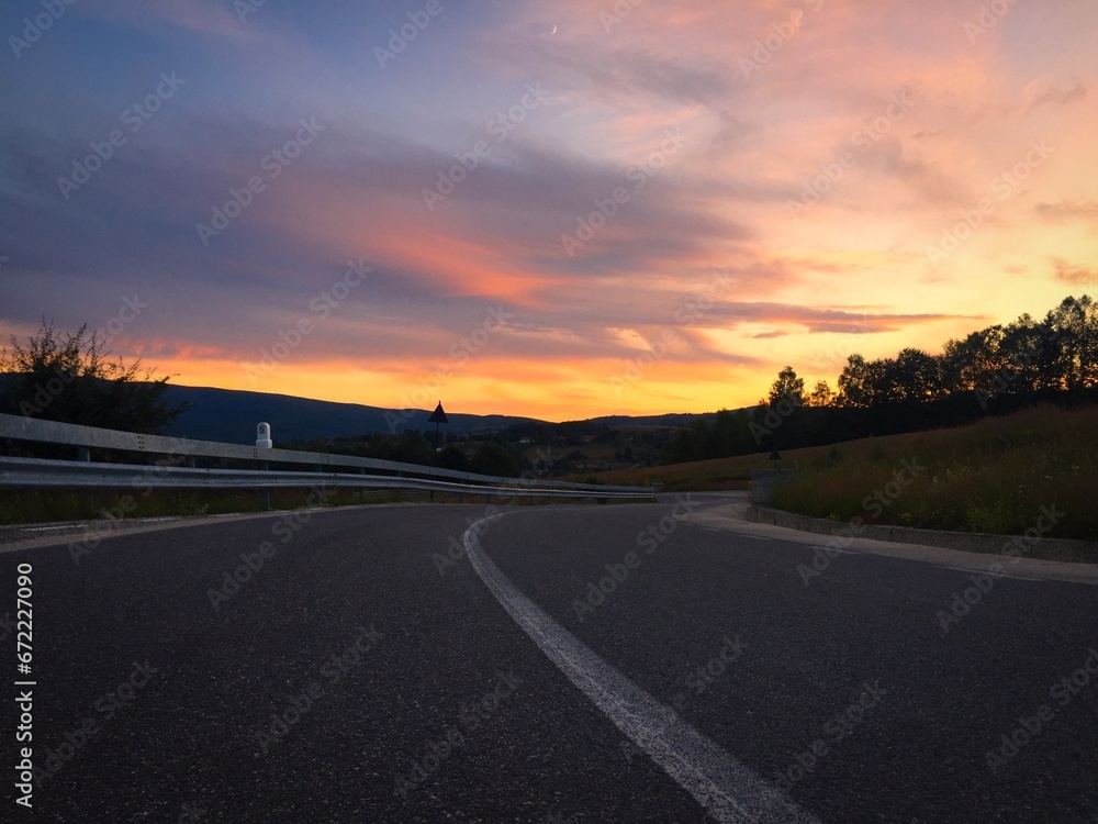 Sunset over an empty road surrounded by the silhouettes of hills and trees