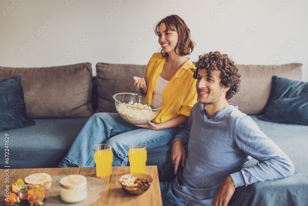 Portrait of young happy couple who is relaxing and watching TV at home.
