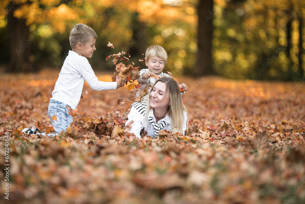 Fototapeta premium Happy young mother and two brothers walking in the autumn forest. Autumn outdoor activity for family with kids. Happy mothers day.
