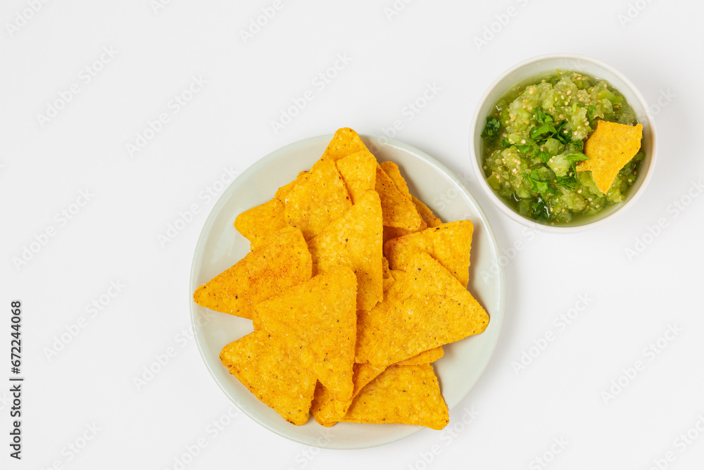 Nachos or triangular corn tortilla chips served with spicy salsa verde sauce top view on white background Nachos or triangular corn tortilla chips served with spicy salsa verde sauce top view on white background