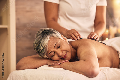 Woman, spa and stone massage for healing back muscle, skincare treatment and holistic therapy at beauty salon. Mature female person relax at wellness resort with rocks for self care, detox and zen