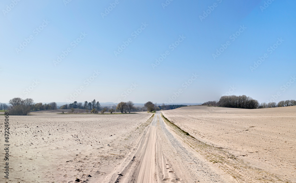 A desolate agricultural farmland caused by summer heat droughts and impact on agriculture industry. Open and empty dry sand. Sandy and barren land with trees in the distance and blue sky background.