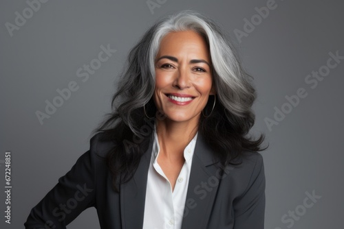 Portrait of a confident elder businesswoman in a suite on the solid grey background with grey hair . Copy space around.