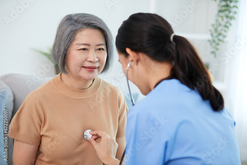 nurse or caregiver using stethoscope to examine senior woman at home