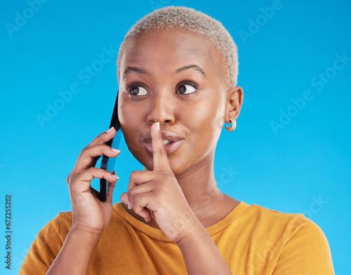 Phone call, secret or finger on lips of black woman in studio for mystery, gossip or conversation. Privacy, news or whisper with girl or shush gesture on blue background for rumor, drama or silence photo