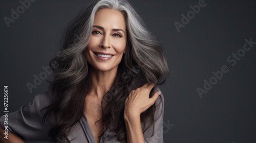 Sensual middle-aged beautiful Asian woman with long grey hair, her eyes closed, body and face care concept. Charming mature lady stands in profile isolated on grey studio background © PaulShlykov