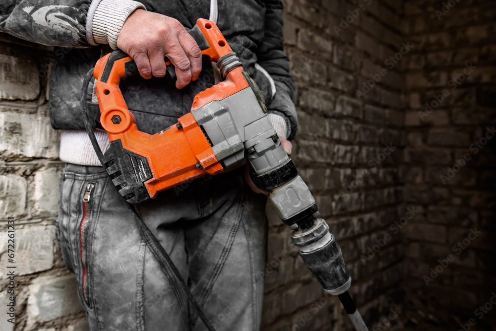 Worker with orange demolition hammer on brick wall background.