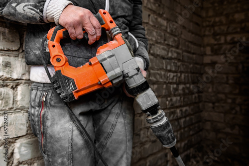 Worker with orange demolition hammer on brick wall background.
