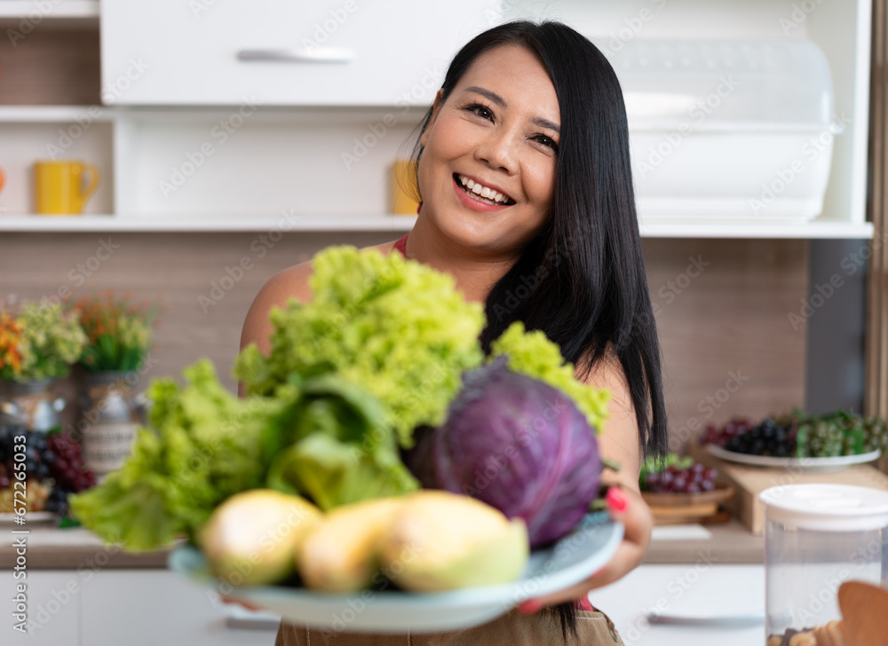 Portrait Happy Asia plus size woman holding vegetables salad in kitchen at home	