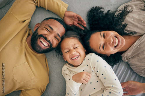 Happy family, above and kid smile or happy with parents together in the morning laughing in a bedroom on a bed. Relax, mom and dad enjoy quality time with kid with happiness, bonding and love photo