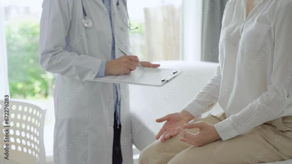 Doctor and patient are in the clinic. Pediatrician is standing and writing medical notes on a clipboard while a young woman is sitting on a sofa. Medicine, healthcare concepts Doctor and patient are in the clinic. Pediatrician is standing and writing medical notes on a clipboard while a young woman is sitting on a sofa. Medicine, healthcare concepts