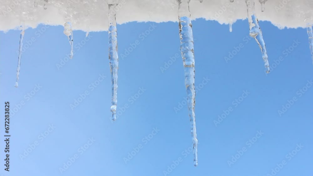 spring drops, a snowdrift with melting icicles hanging from the roof against the blue sky spring drops, a snowdrift with melting icicles hanging from the roof against the blue sky