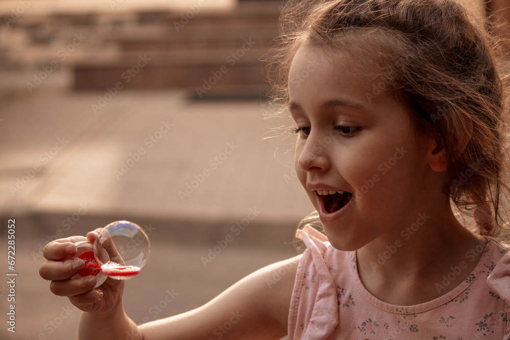 A little girl with red or brown hair blows soap bubbles. The concept of a carefree, happy, peaceful childhood. Close-up, happiness A little girl with red or brown hair blows soap bubbles. The concept of a carefree, happy, peaceful childhood. Close-up, happiness