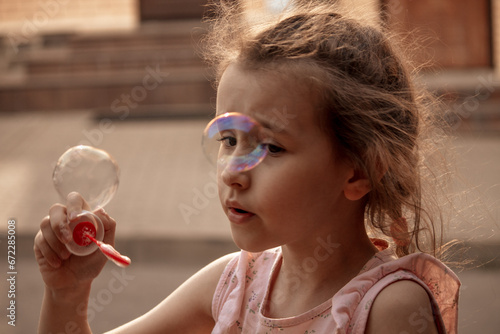 A little girl with red or brown hair blows soap bubbles. The concept of a carefree, happy, peaceful childhood. Close-up, happiness