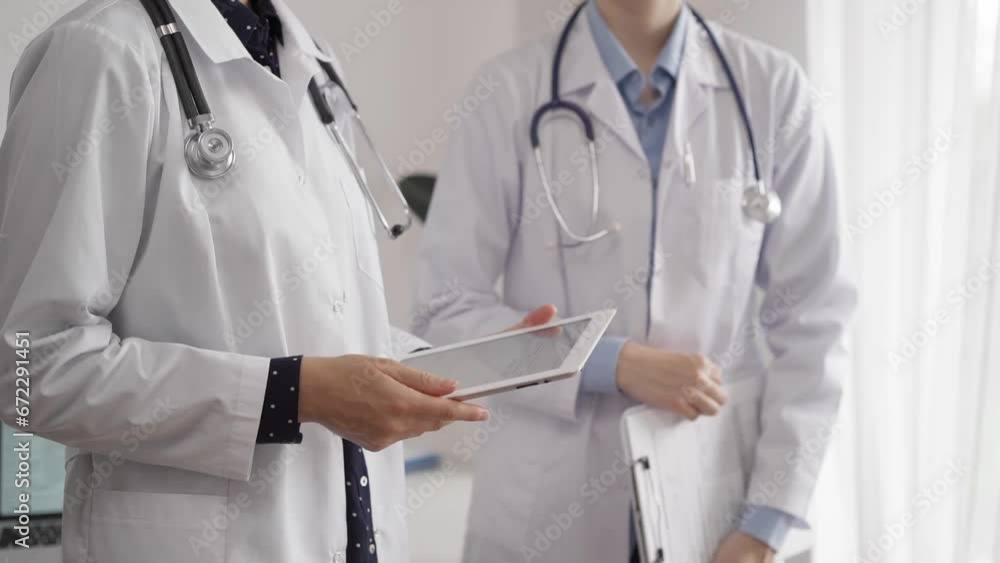 Two female doctors are using a tablet computer while standing and discussing health treatment in a hospital. Medicine concept Two female doctors are using a tablet computer while standing and discussing health treatment in a hospital. Medicine concept