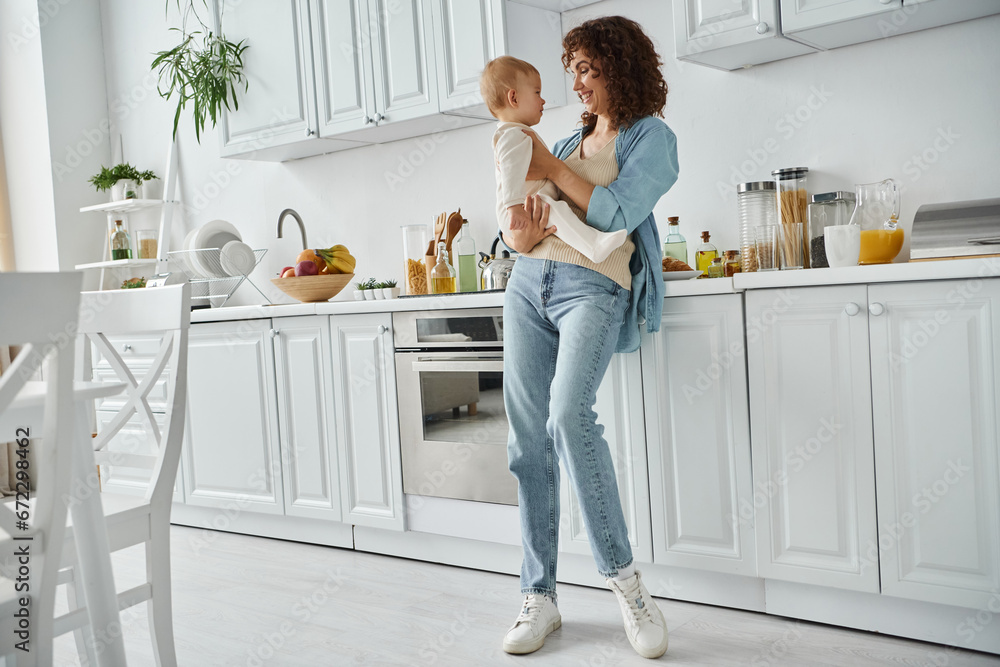 full length of happy woman holding little daughter in spacious modern kitchen with white furniture full length of happy woman holding little daughter in spacious modern kitchen with white furniture