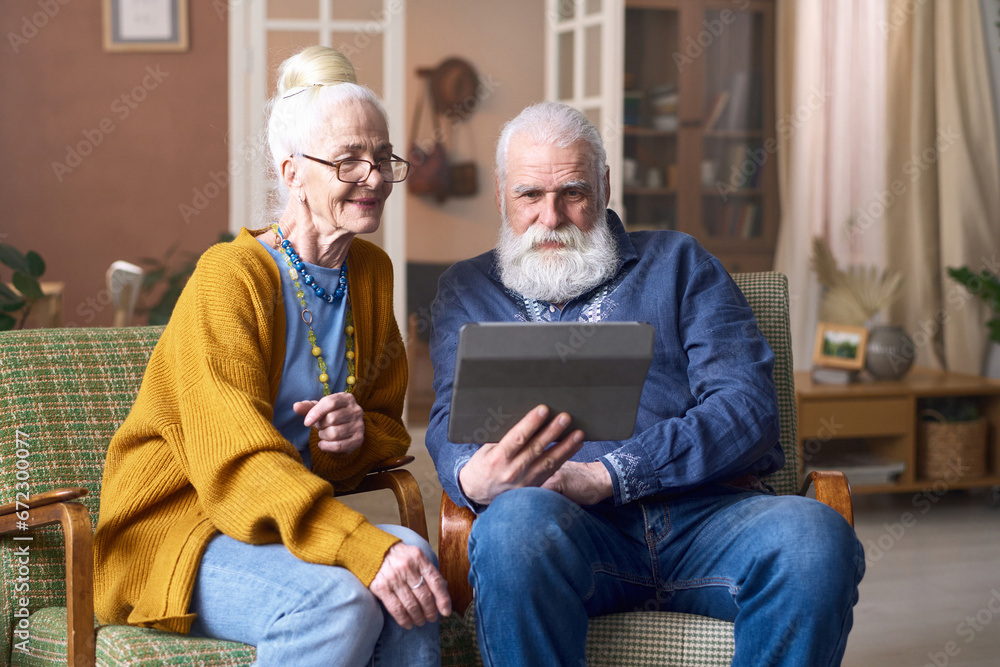 Senior couple watching video on tablet pc while sitting on armchairs in the living room