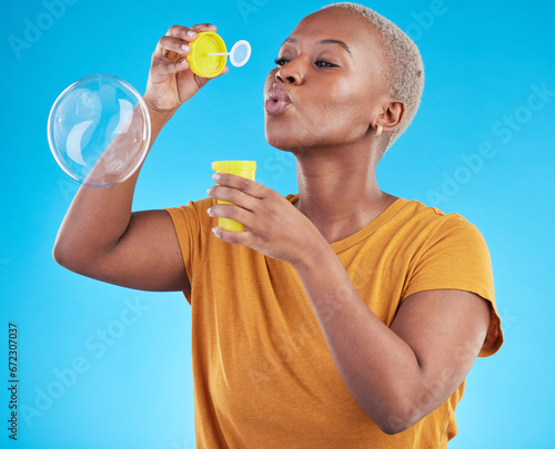 African, woman and blowing bubbles in studio, blue background or fun party celebration with liquid soap or toy. African girl, person and relax with happy, joyful or creative bubble for calm break