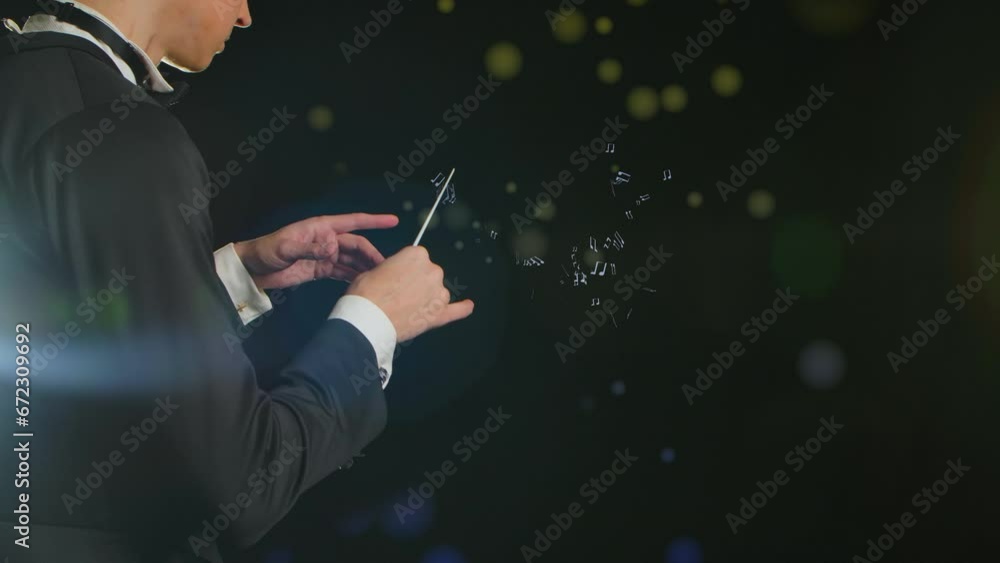 In a close up shot, a man in a tuxedo stands against a black background. He is a conductor and conducts with a baton. Multi-colored notes and a treble clef float around him. Demonstrates musical art In a close up shot, a man in a tuxedo stands against a black background. He is a conductor and conducts with a baton. Multi-colored notes and a treble clef float around him. Demonstrates musical art