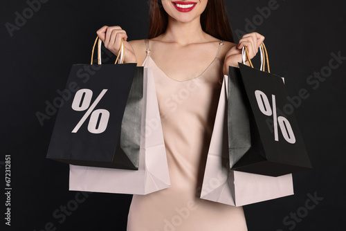 Discount, sale, offer. Woman holding paper bags with percent signs against black background, closeup