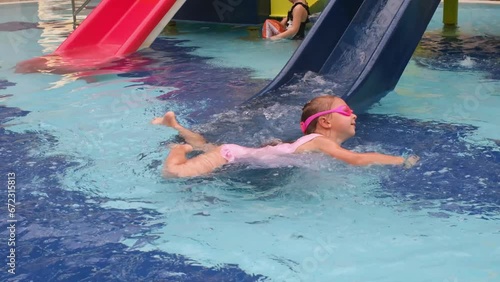 Child sliding into the water in aqua park. Kid having fun and entertaining in indoor swimming pool. Toddler girl making splashes 