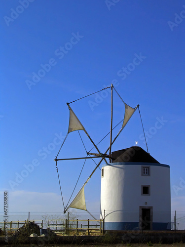 Typical Portuguese windmill from the central and southern regions in Sesimbra, Portugal. View of the cloth sails partially unwrapped from the masts. Backlit silhouette.