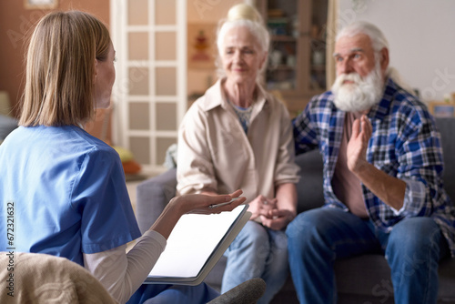 Rear view of young social worker talking to senior couple in the living room at home