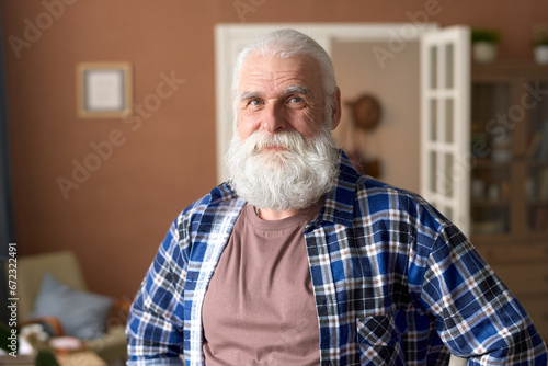 Portrait of senior man with white beard looking at camera while standing in the room