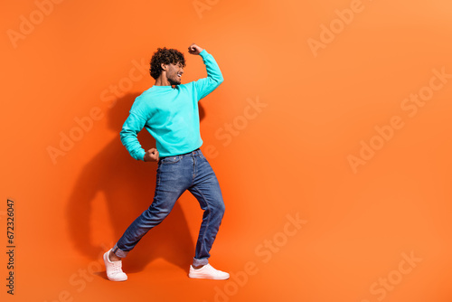 Full body profile portrait of astonished glad handsome guy raise fists empty space isolated on orange color background