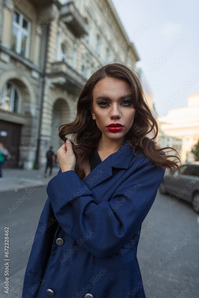 Glamorous beautiful fashion girl with makeup and hairstyle in a fashionable blue suit walks on the street and looks at the camera Glamorous beautiful fashion girl with makeup and hairstyle in a fashionable blue suit walks on the street and looks at the camera
