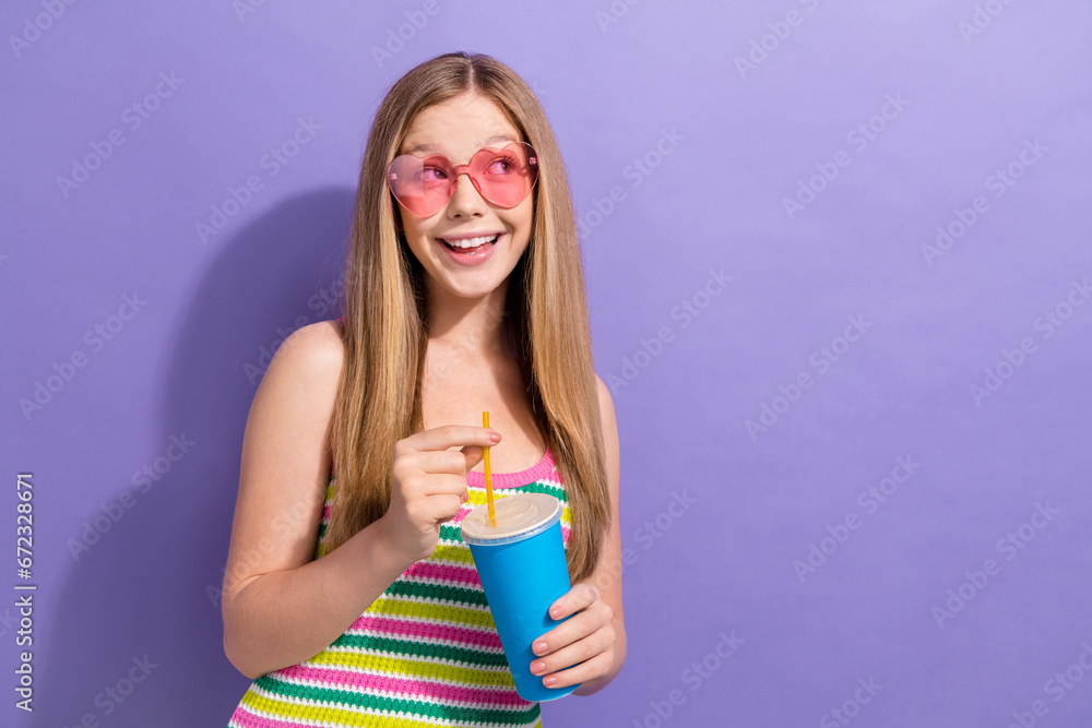 Photo portrait of lovely teen blonde lady look empty space drink soda dressed stylish striped garment isolated on violet color background