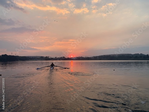 Rowers on flat water into a pink sunset