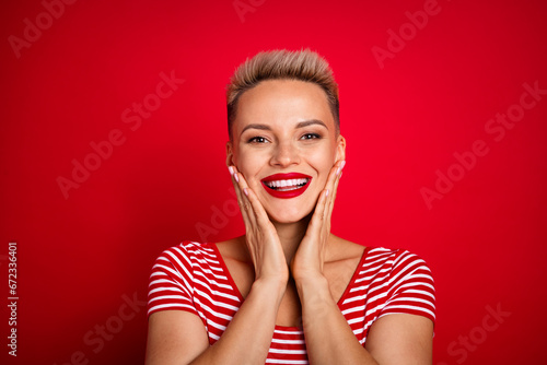 Photo of lovely adorable girl wear stylish clothes two arms touch cheeks showing white teeth visage isolated on red color background