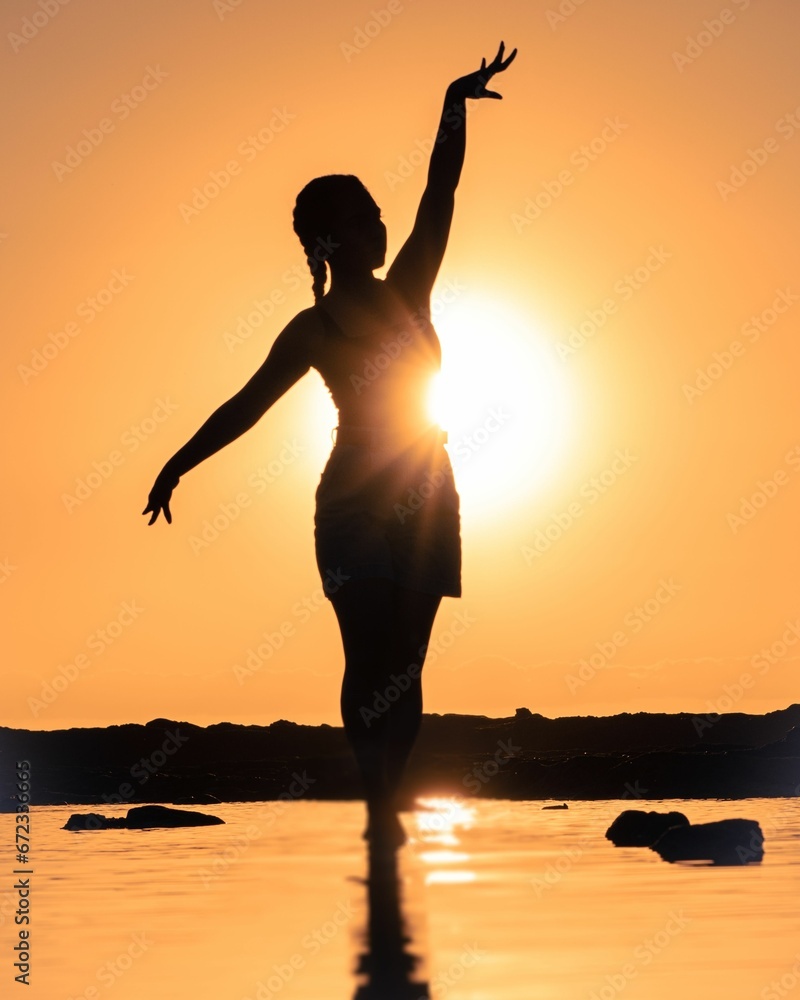 Stunning silhouette of a woman in yoga gear stretching out her arms against a sunset backdrop