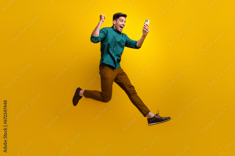 Fototapeta premium Photo of overjoyed cheerful man dressed stylish clothes going running reading sms isolated on yellow color background