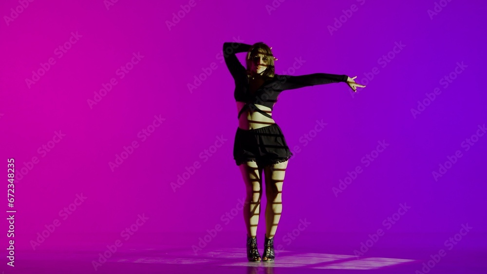 Attractive woman dancing heels dance in a studio. Blue to purple neon gradient background, striped falling shadow. Black sexy costume, high heels. Modern sensual choreography. Full length.