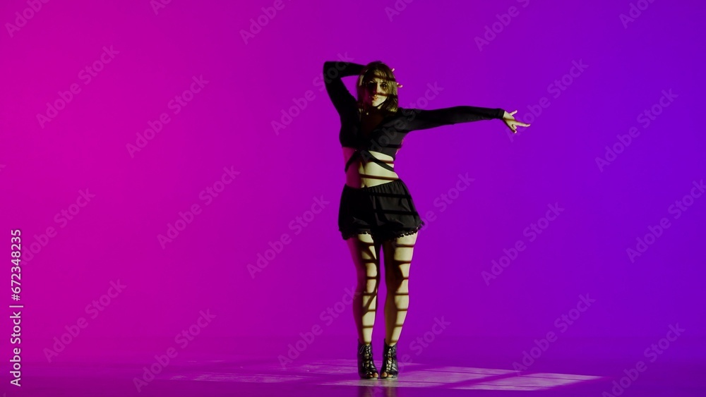 Attractive woman dancing heels dance in a studio. Blue to purple neon gradient background, striped falling shadow. Black sexy costume, high heels. Modern sensual choreography. Full length. Attractive woman dancing heels dance in a studio. Blue to purple neon gradient background, striped falling shadow. Black sexy costume, high heels. Modern sensual choreography. Full length.